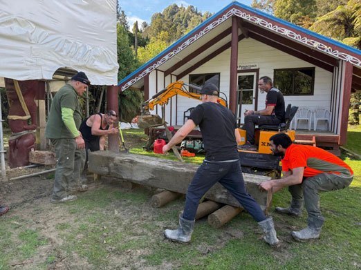 Whānau moving the pou whenua in front of the wharenui at Tieke